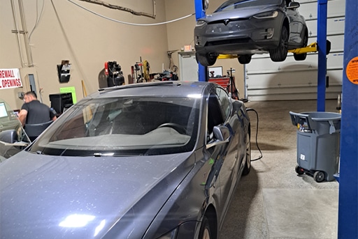 Tesla EV Repair specialists in Wake Forest and Raleigh, NC with Pleasant Automotive. Image of gray Tesla sedan being re-charged after maintenance services and another gray Tesla in the air on a lift in the shop for brake and maintenance services in the shop.