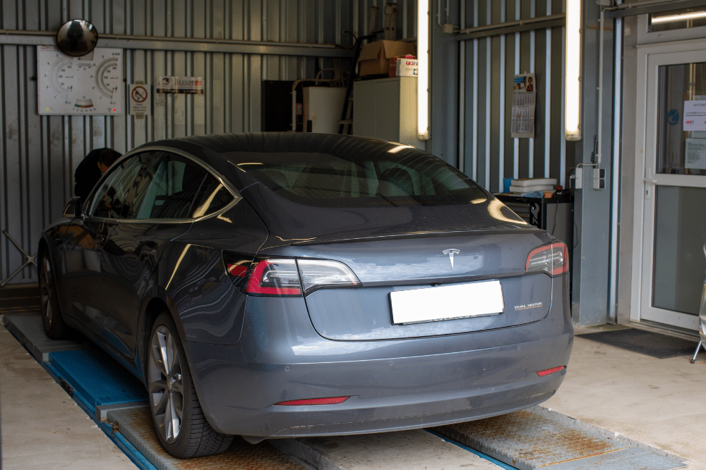 Tesla Maintenance Schedule in Wake Forest, NC by Pleasant Automotive. Tesla Model 3 in a service garage undergoing maintenance inspection, representing trusted Tesla care and service.