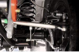 Suspension in Wake Forest, NC by Pleasant Automotive. Close-up of a vehicle's front suspension system showing the coil spring, control arm, and steering linkage components.